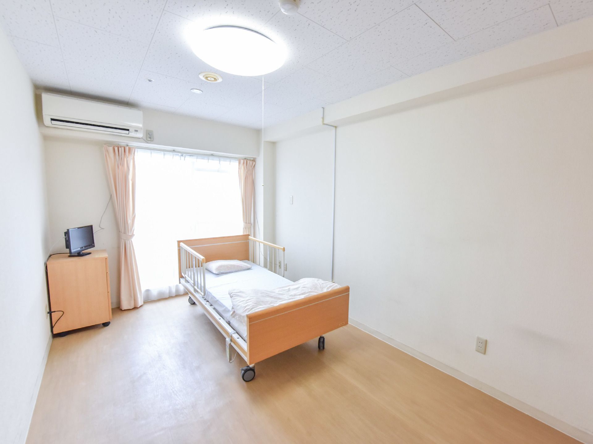 清潔感のある明るい居室である。エアコンが設置されており掃き出しの窓にはレースのカーテンが掛けられている。