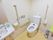 清潔感のあるトイレである。便器に蓋がなく、壁にはL型の手摺が設置されており、便器の横には可動式の手摺がある。