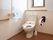 小窓のある明るい個室トイレで、床は木目調のフローリングになっている。温水洗浄機能付きの便座で、壁には手すりが設置されている。