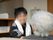 白いタオルを巻いた男性スタッフと入居者様が親しげに会話をしている。奥の壁に、ホワイトボードが掛けられている。