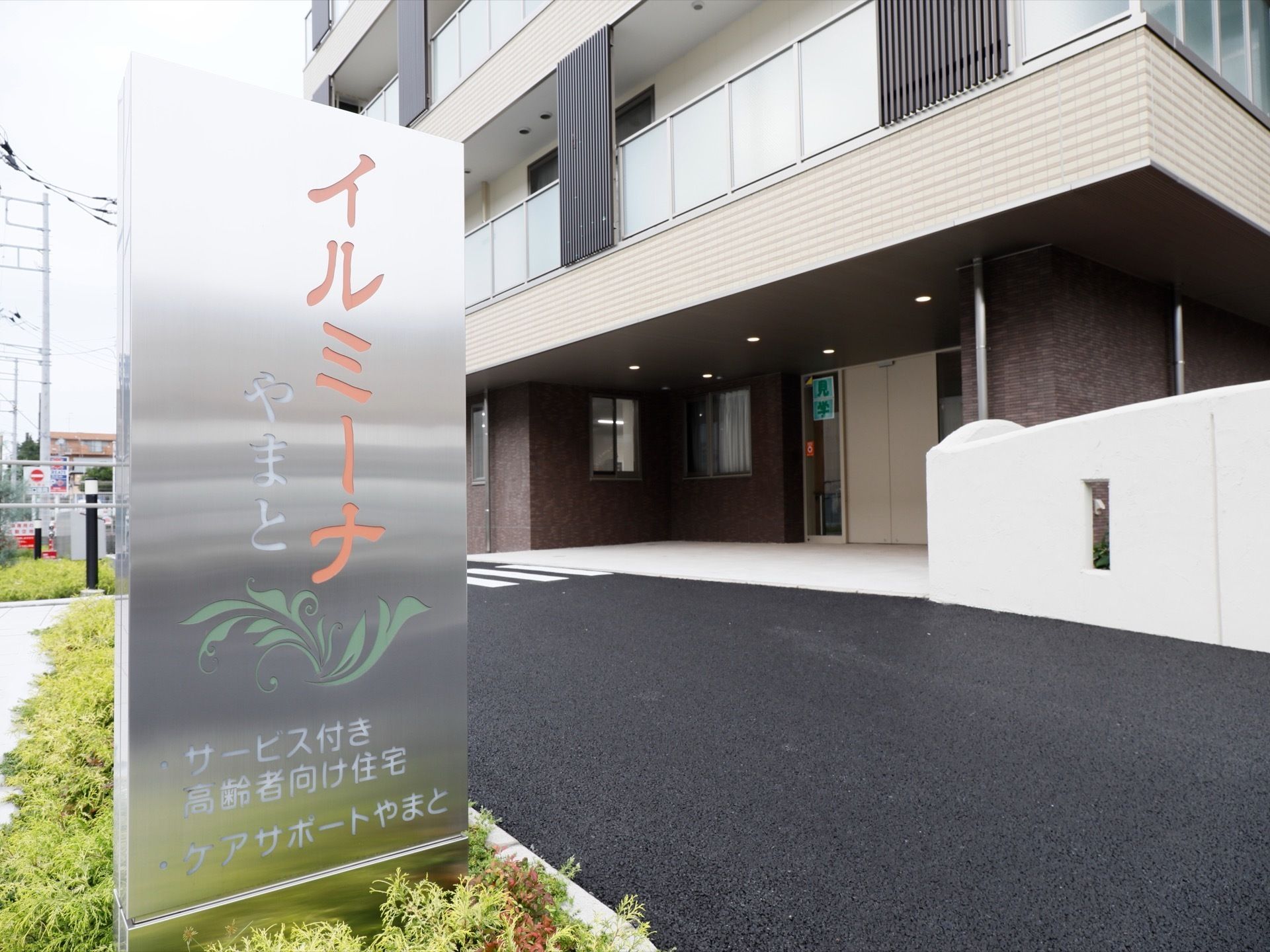 施設の入り口前には植え込みがあり、その中に施設名を書いた長方形の看板を設置している。玄関前はアスファルト舗装である。