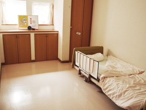 介護ベッドの置かれた室内で、作り付けのクローゼットや収納棚がある。白い壁と明るい茶色の木でまとめられている。