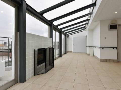 ルーフバルコニーはガラス張りになっており、明るい雰囲気である。周囲の壁は白色系で手すりが設置されている。