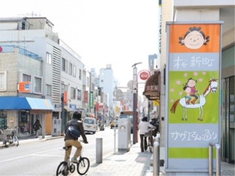 地域の商店街の外観である。道の両側には商店が立ち並び、歩道の看板には、漫画のキャラクターのイラストが描かれている。