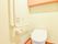 手すりがついた洋式のトイレがあり、ウォシュレットになっている。上部には木製の収納棚があり、観音開きである。