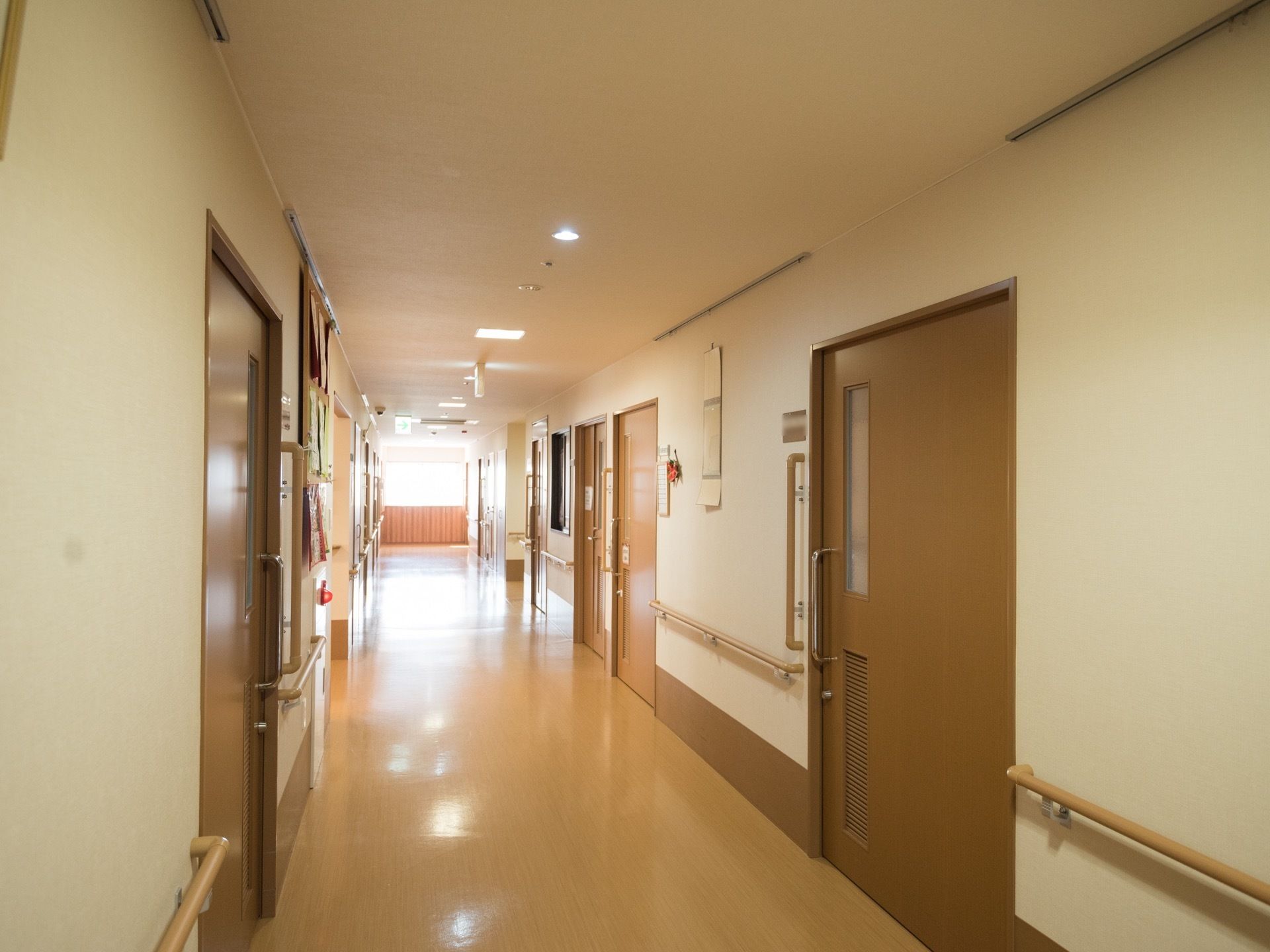 廊下は、ビニール素材の床面になっている。居室入口の取っ手の近くの壁に、縦方向の大きな手すりが設置されている。