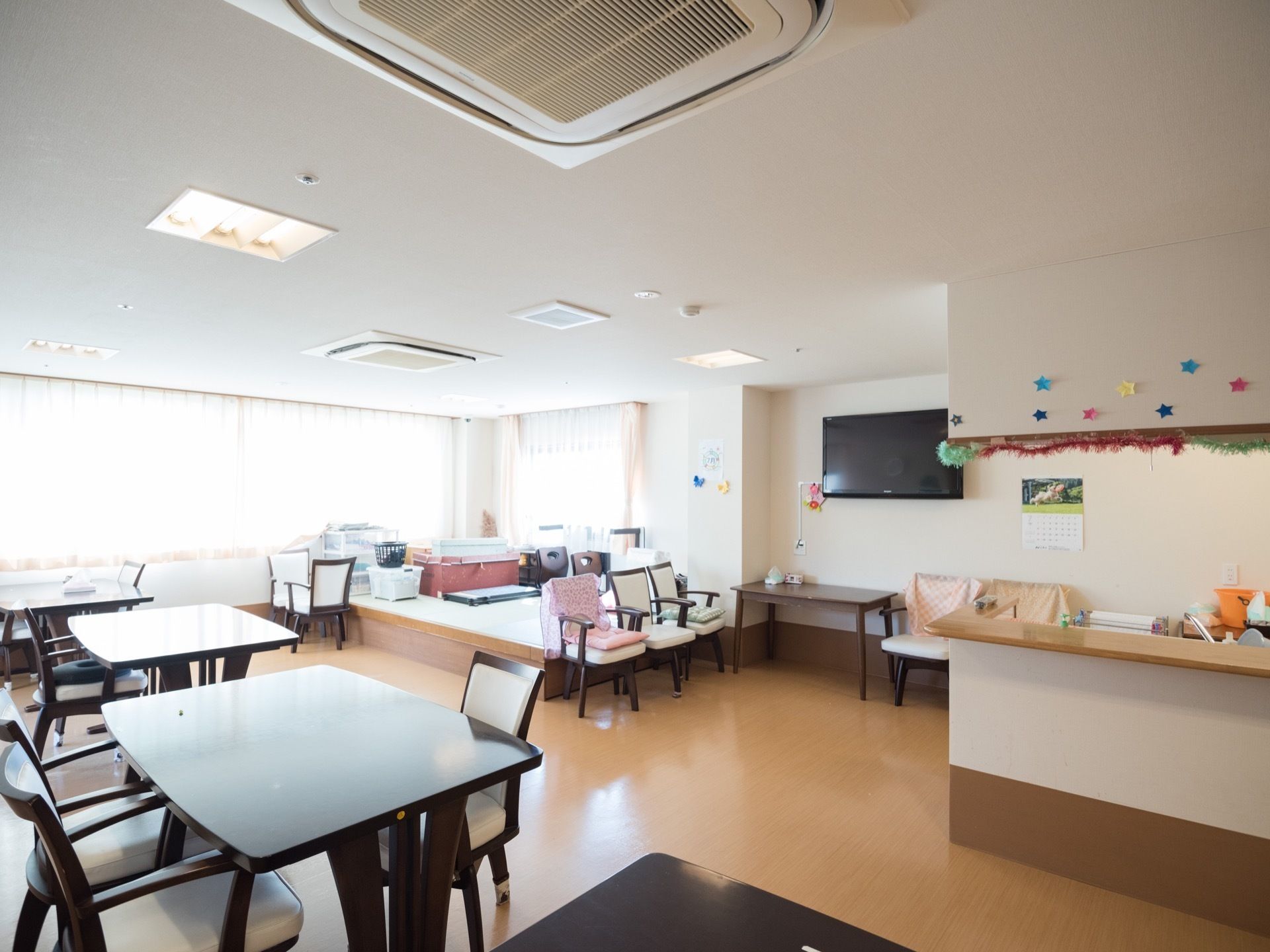壁一面の窓があってとても明るい食堂です。天井埋め込み式のエアコンが２台設置されている。一段高くなった畳のスペースもある。