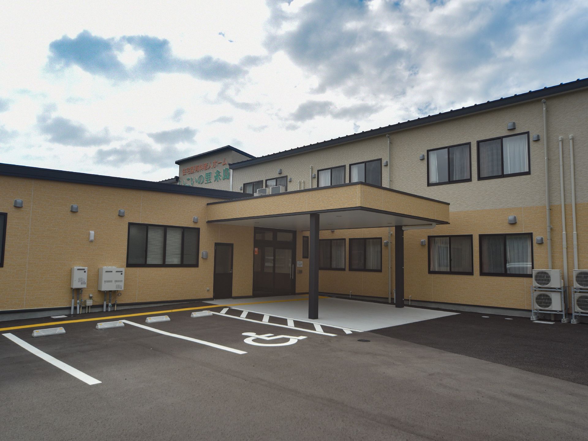 2階建てのホームの中央付近には、オレンジ色と緑色の大きな文字で施設名が書かれている。外装は、ベージュ系の色である。