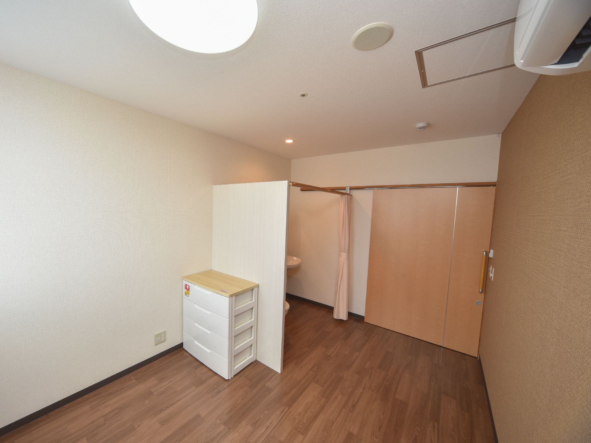部屋の出入り口には、大きな引き戸が設置されている。白い壁の前には、プラスチック製の収納ケースが置かれている。