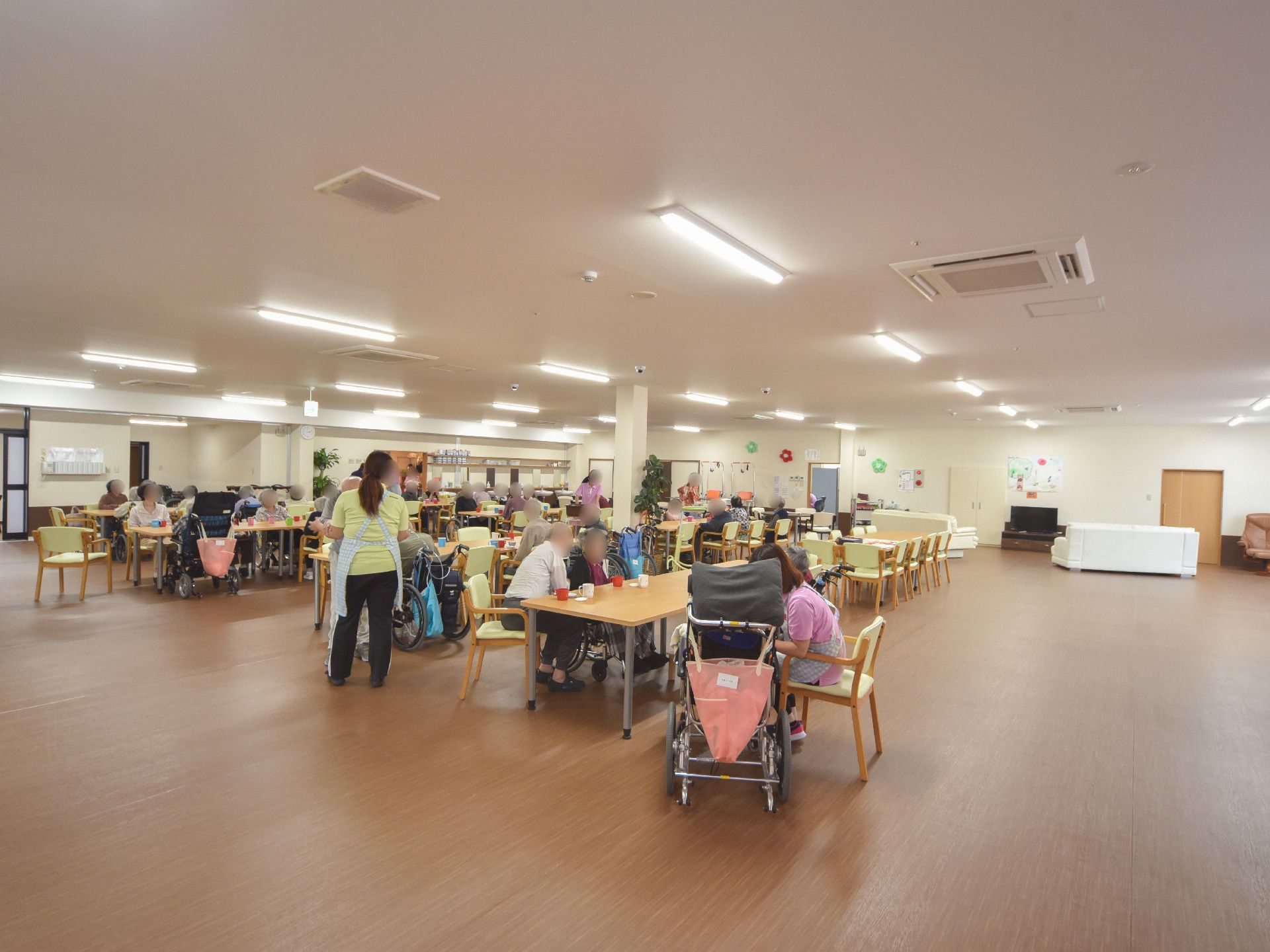 天井にはたくさんの照明器具が付いていて、広々とした空間を明るく照らしている。奥の方には、白いソファーとテレビが置いてある。