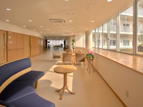 廊下途中に設けられた日当たりの良いラウンジである。テーブルやソファが複数設置されており、壁際には花が飾られている。