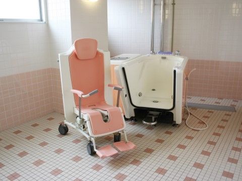 白とピンクのタイル張りの浴室に介護入浴用の浴槽と車椅子が置かれている。入居者様は座ったままの姿勢で入浴できる。