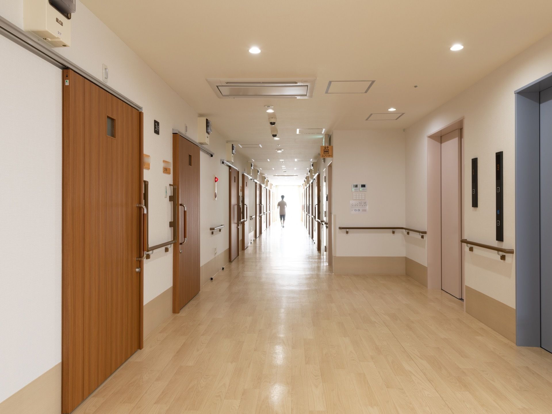 通路の両側にはスライド式ドアが設置された居室が並んでいる。淡いベージュとブルーの扉のエレベーターが２基設置されている。