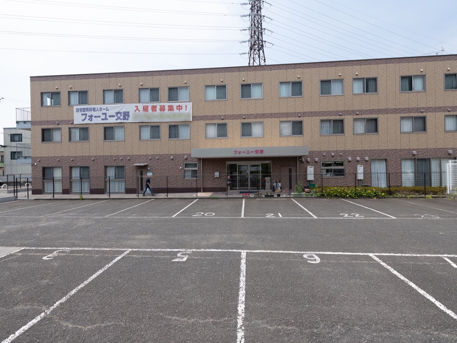 施設は、濃いベージュ色を基調とした落ち着いた雰囲気である。２階と３階の間には施設名が大きく書かれた入居者様募集の幕が掛けられている。