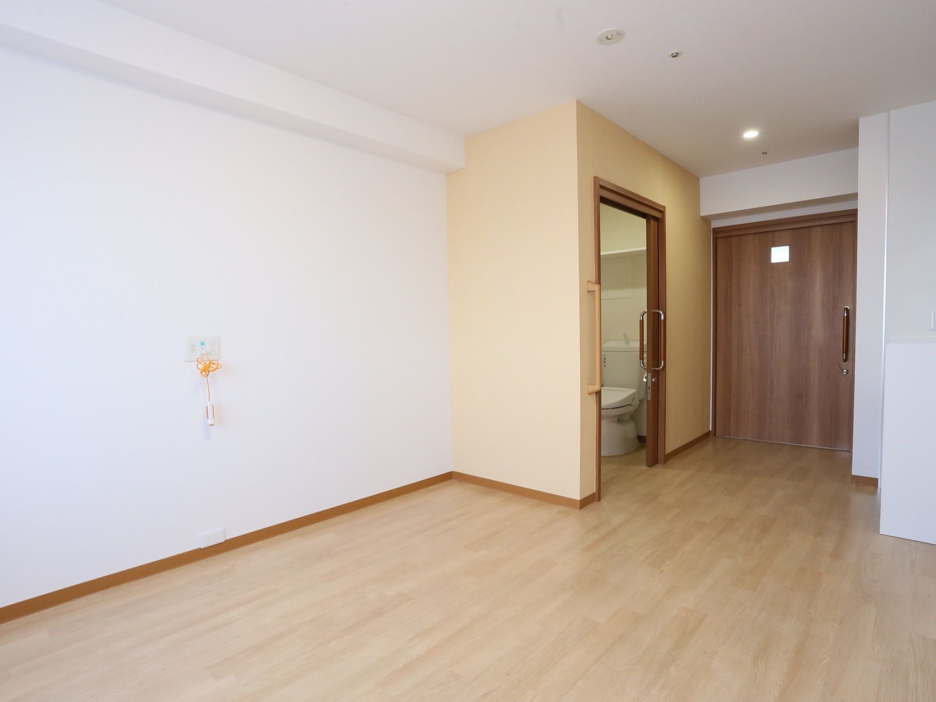 天井と壁が白で、床がフローリングの広い部屋である。壁にはナースコールが設置されている。奥にトイレが見える。