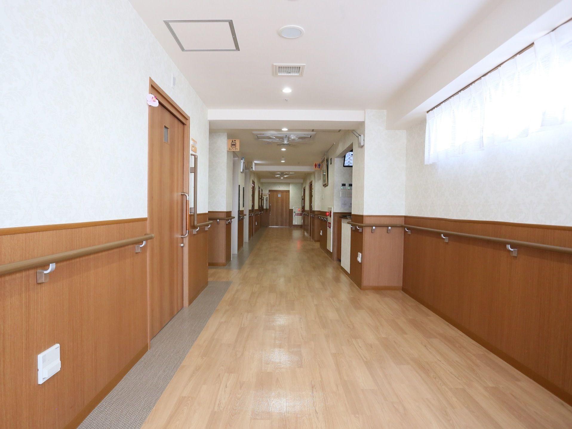 横幅の広い廊下である。壁は腰高の位置まで木目調となっており、壁伝いに手すりが取りつけられている。居室の入口ドアは引き戸式となっている。