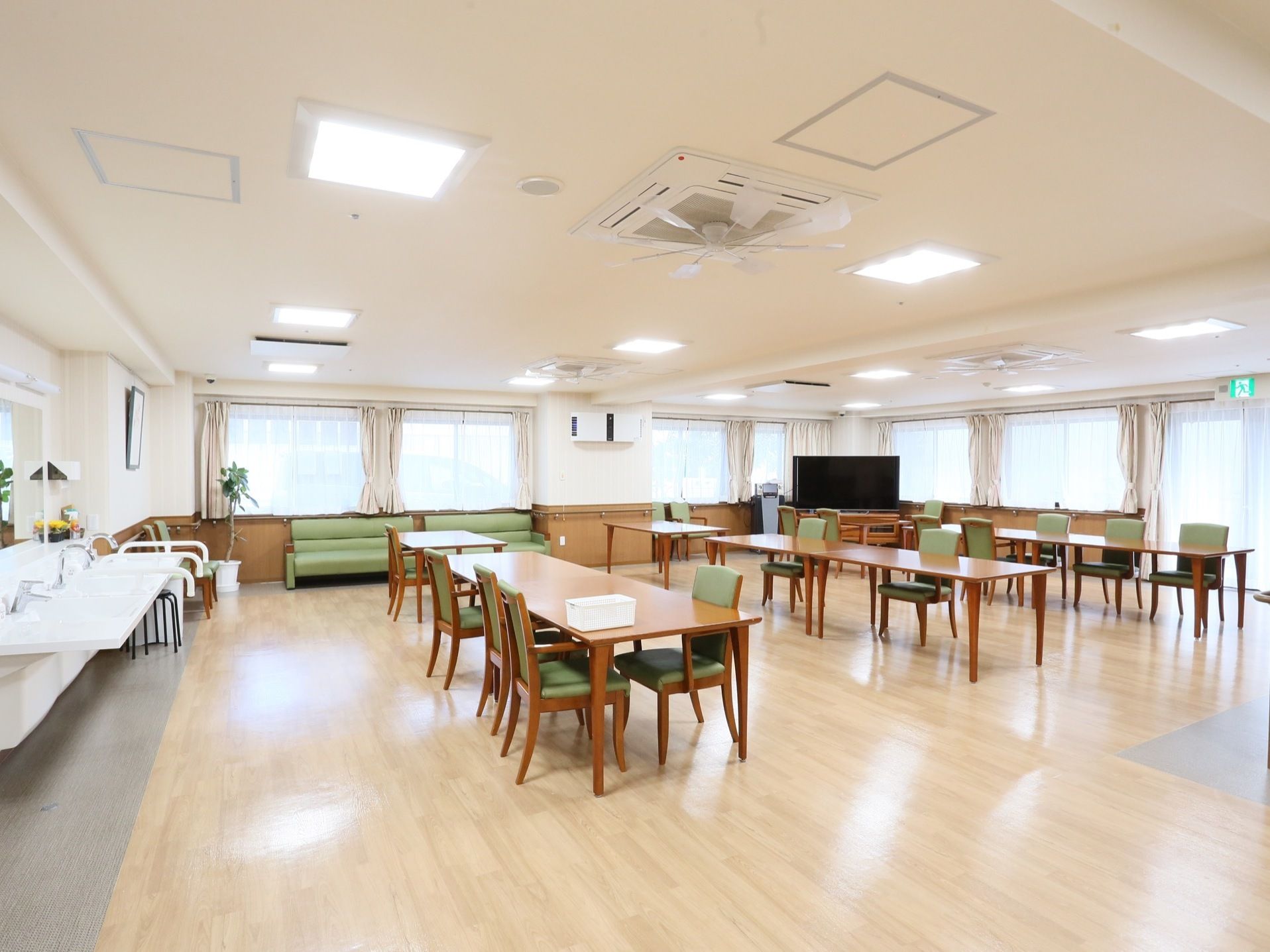 壁際に洗面台が設置されている。奥にはソファが置かれている。中央には、テーブルと椅子のセットが数組配置されている。