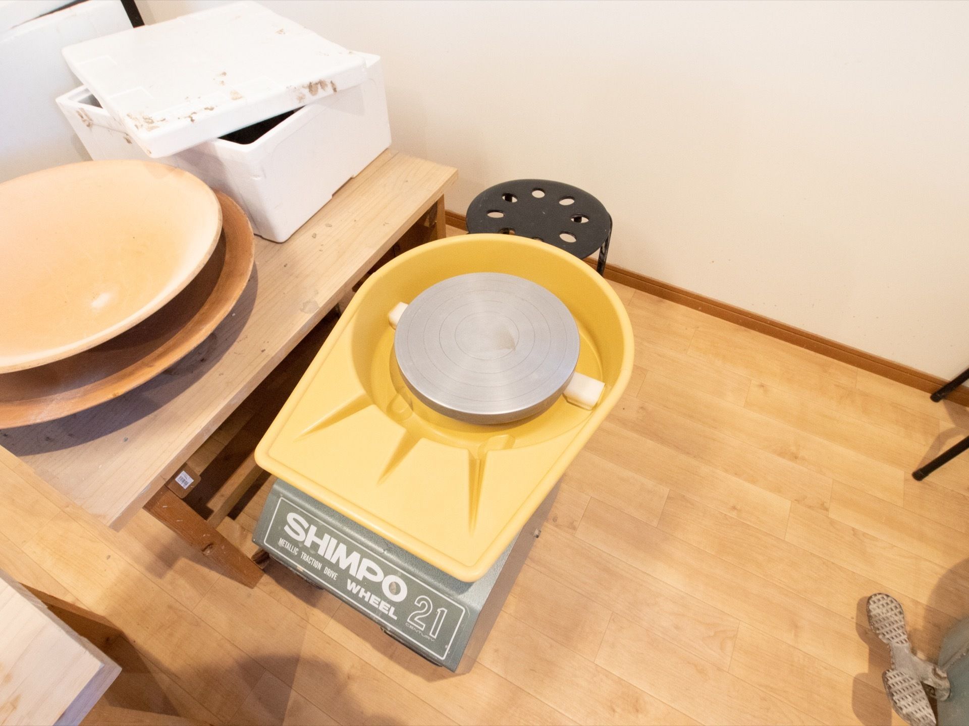 フローリングの部屋に、電動ろくろと椅子が置かれている。作業台の上には発泡スチロールと作りかけのお皿がある。