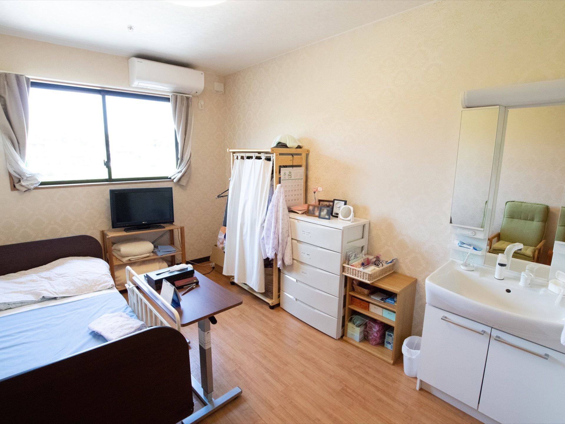 フローリングの部屋に、ベッド、タンスや書き物デスクなどがある。洗面台とエアコンが備えつけられている。