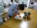 大きなテーブルの上に白いまな板が置かれ、入居者様がニンジンを細かく切っている様子である。まな板の近くにはステンレスの鍋が置かれている。
