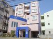 建物の周辺には、マンションが建ち並んでいる。建物は薄いベージュ色でところどころ、濃い青色で縁取られている。