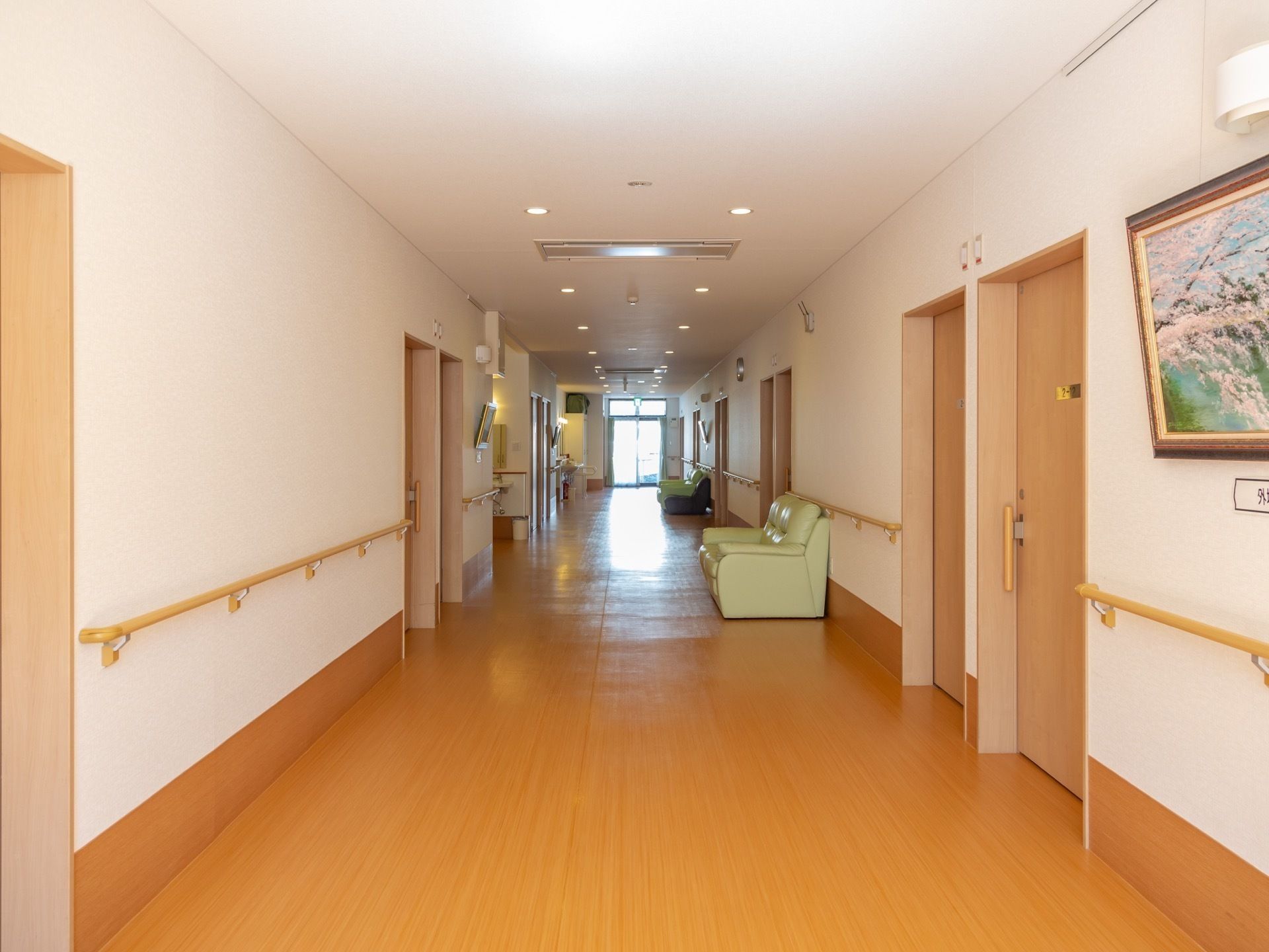 木目調の床に白色の壁、天井というデザインで、壁沿いに手すりが設けられている廊下