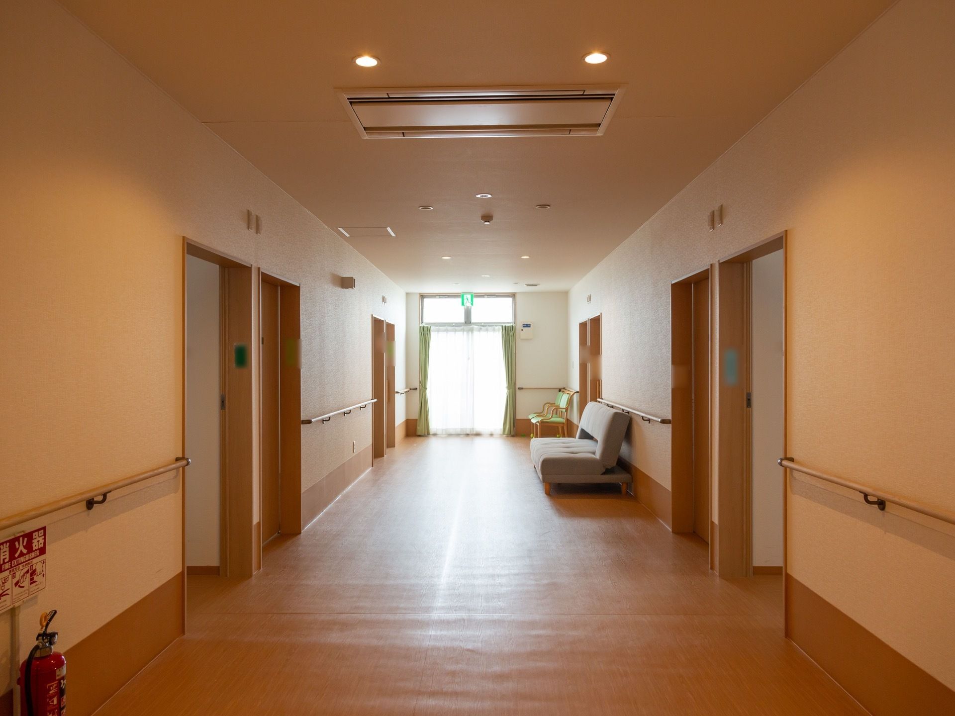 幅の広い通路にソファーが置いてあり、突き当りにカーテンが掛けられた窓がある。天井にダウンライトとエアコンが設置されている。