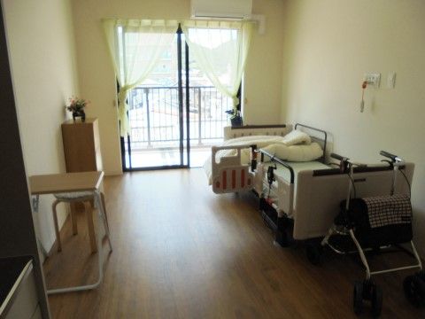 木目調の床と白色の壁、床というデザインで、ベッドやエアコン、ナースコールなどが設置されている居室
