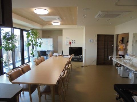 中央に机やテーブルが置かれ、出入り口付近に洗面台がある共有スペース