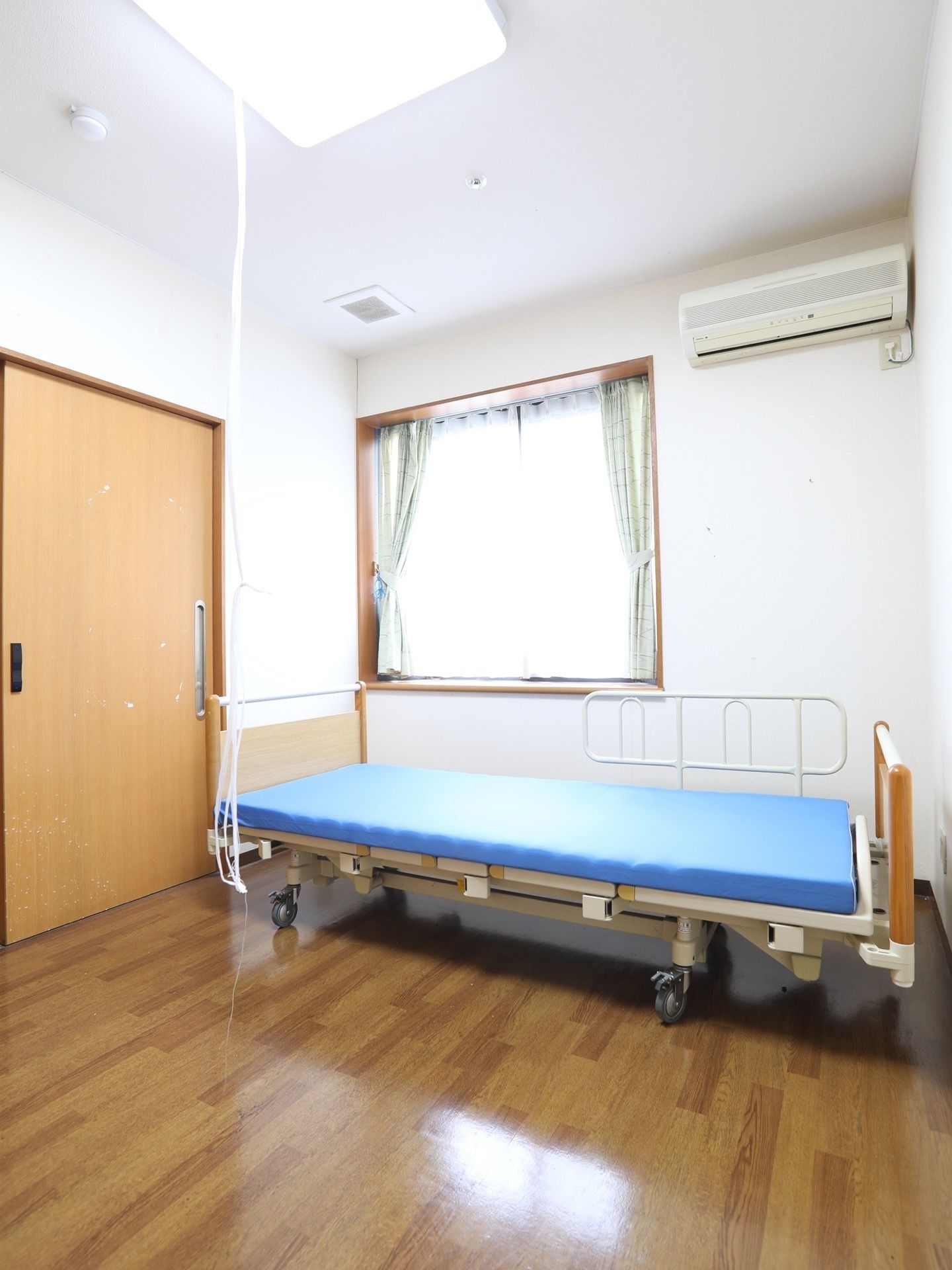 床と扉が木目調で統一された部屋である。日の光の入る窓とエアコンがあり、明るく快適に過ごすことができる。