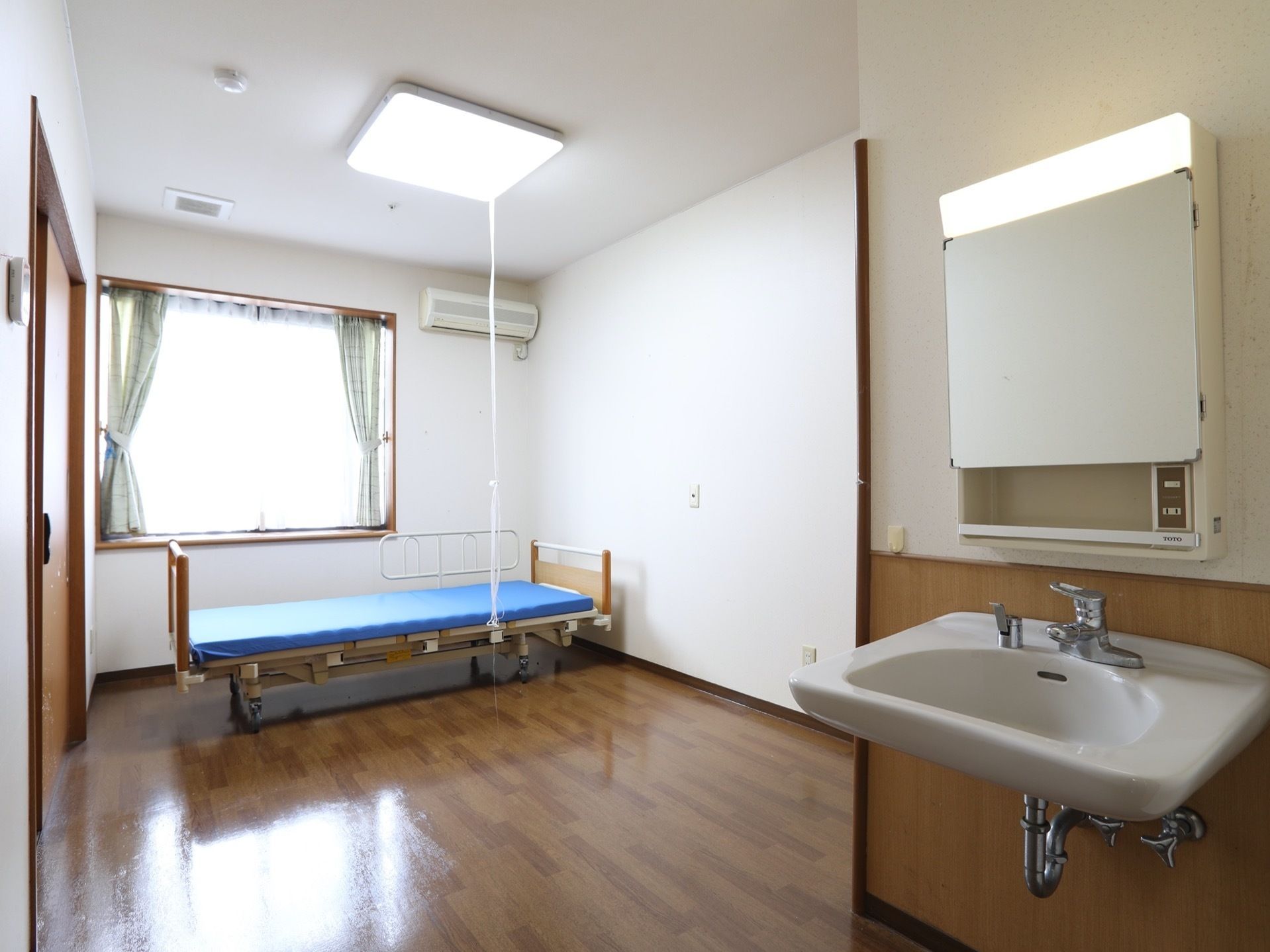 室内に洗面台のある部屋である。窓の近くにはベッドとエアコンが完備され、快適に過ごせるよう配慮されている。