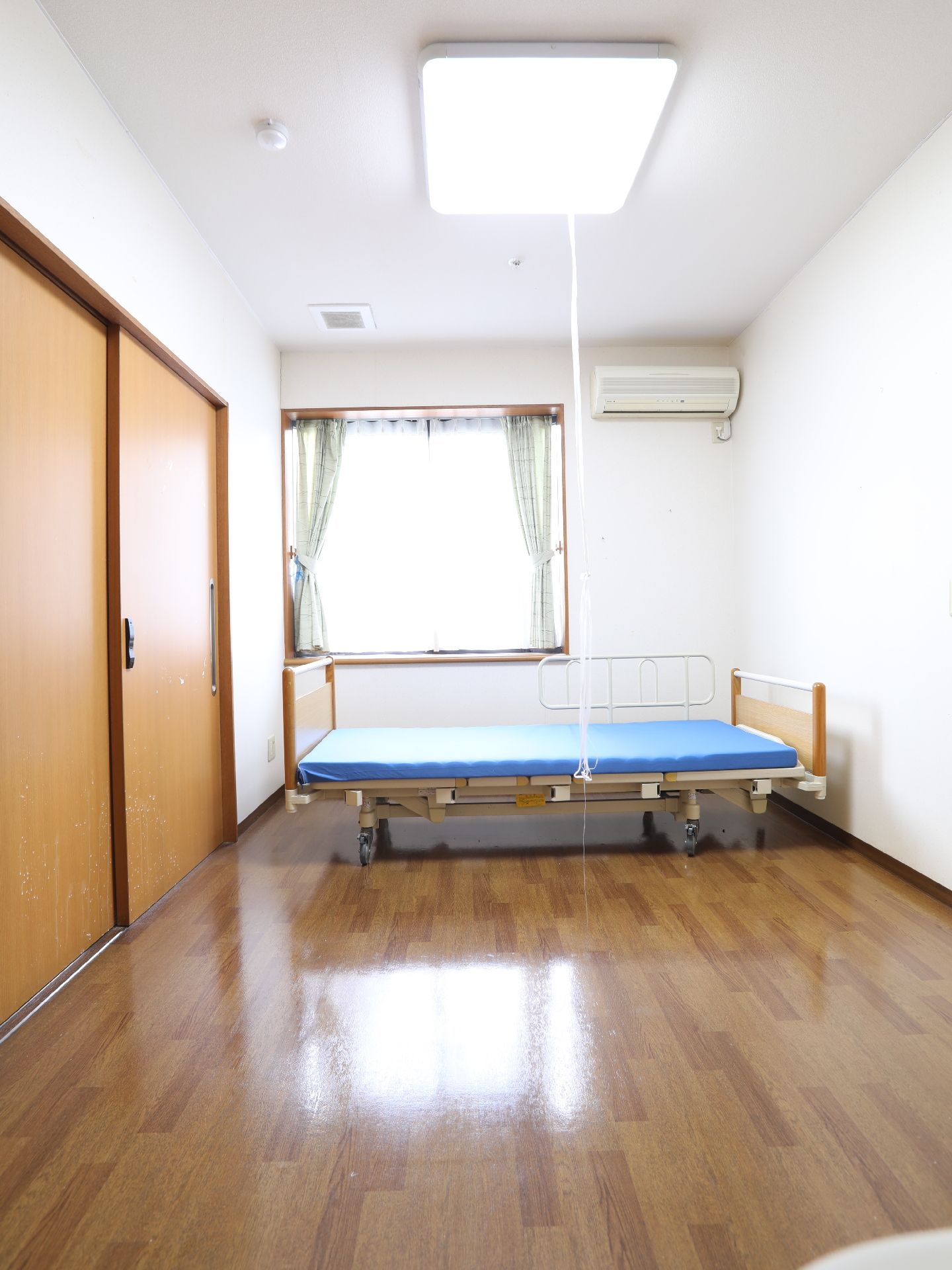 介護用ベッドやエアコンが設置され、天井中央に大きな照明が付いている居室