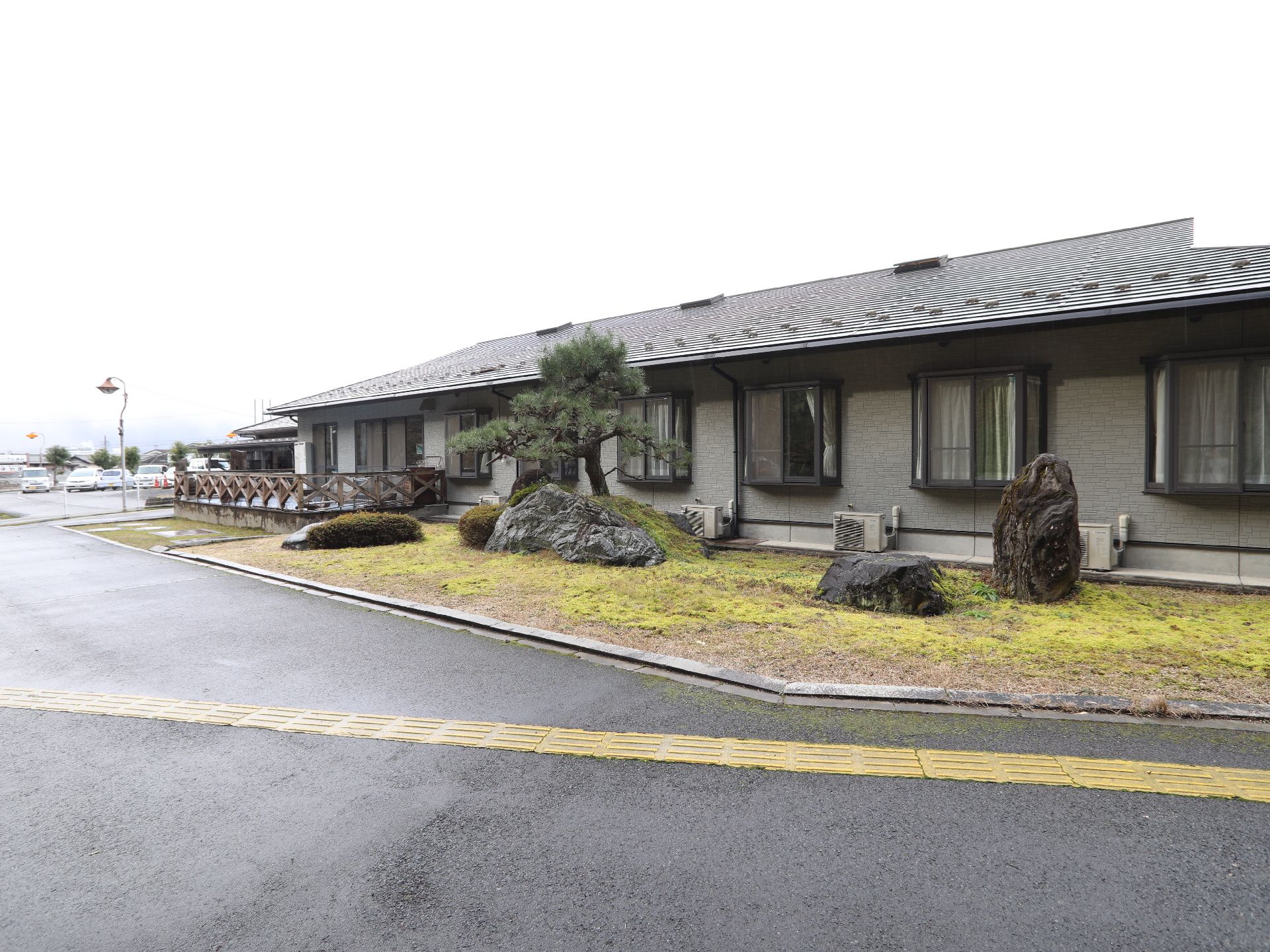 大きな石が置かれ、松の木が生える庭がそばにある平屋建ての建物