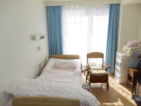 ベッドや椅子が設置された窓から自然光の入る居室
