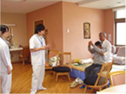 三人のスタッフに見守られながら腕を上げる体操をしている男性