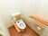 白に木目調を取入れたトイレスペースである。便座にはひじ掛けと背もたれを備えている。横側の壁に棚を設け、手すりを設置している。