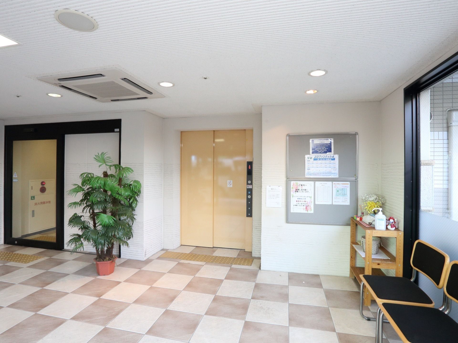 壁際に椅子が並べられ、壁には掲示板が貼られている。エレベーターが設置されていて、その前には点字ブロックの停止線がある。