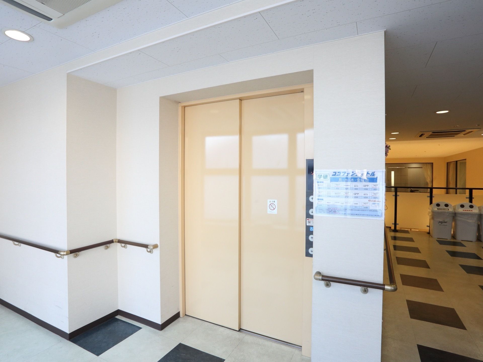 車椅子用ボタンが設置された、大きなエレベーターである。エレベーターまでの通路の壁には、手すりが付いている。