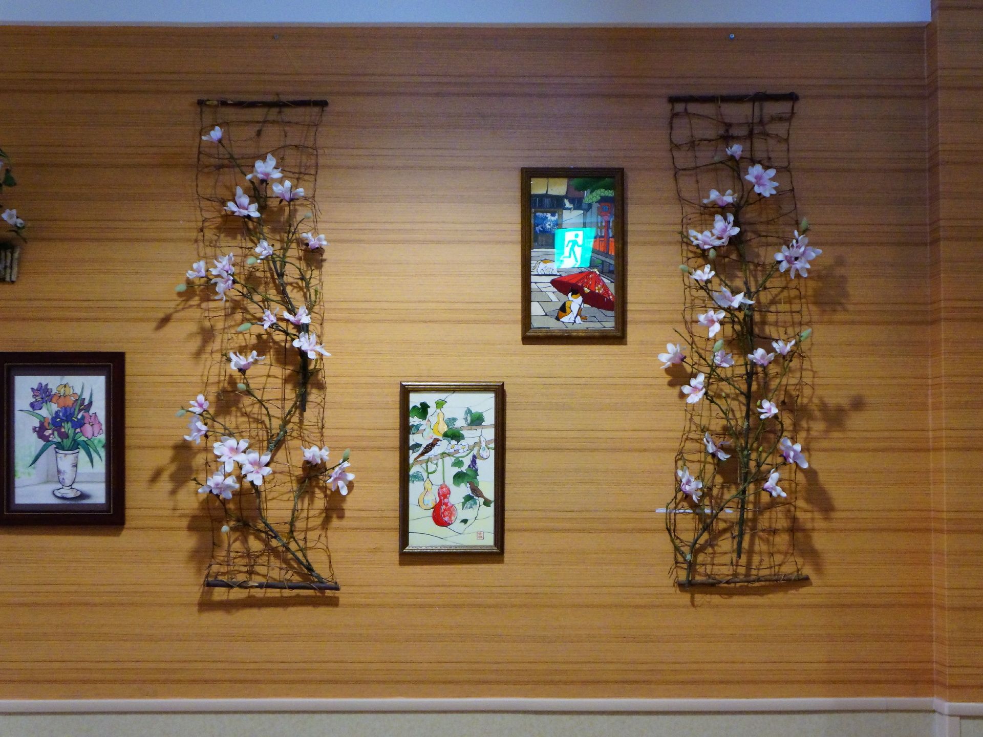 施設の壁には、入居者の手作りの絵画が3点木製のフレームに収められて、展示保存されている。造花の花も展示されている。