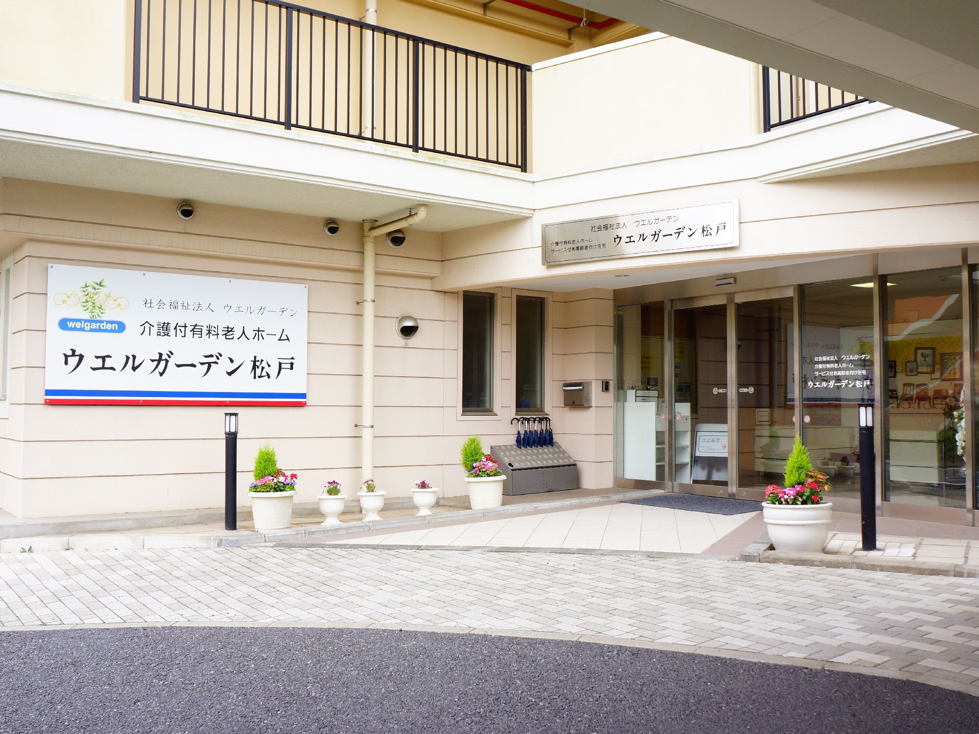 壁に大きな看板がかかり、プランターの花で飾られたエントランス