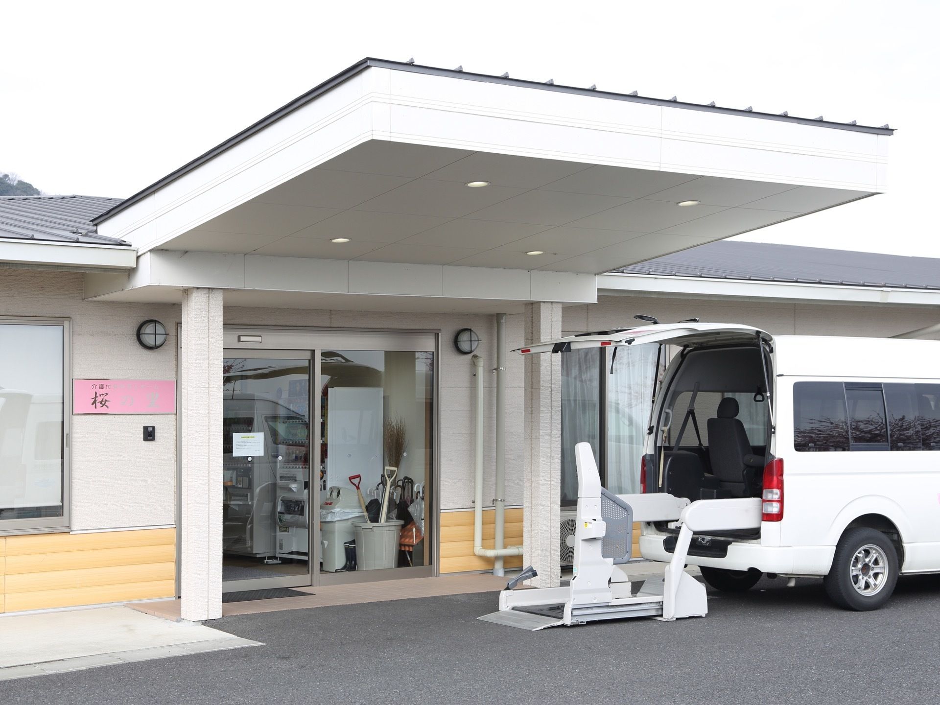 屋根付きの玄関で、外壁には施設名が書かれたピンク色の表札が取り付けられている。館内までのアプローチには段差がない。
