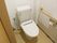白を基調とした温水洗浄機能付きのトイレである。壁には、頑丈な手すりとシンプルな操作パネルが設置されている。