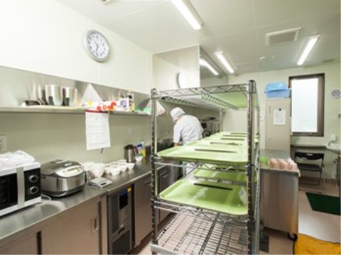 銀色の調理台が壁側に一列に設置されている。床はオフホワイトで清潔感があり、マットを敷いて滑りを抑えている。