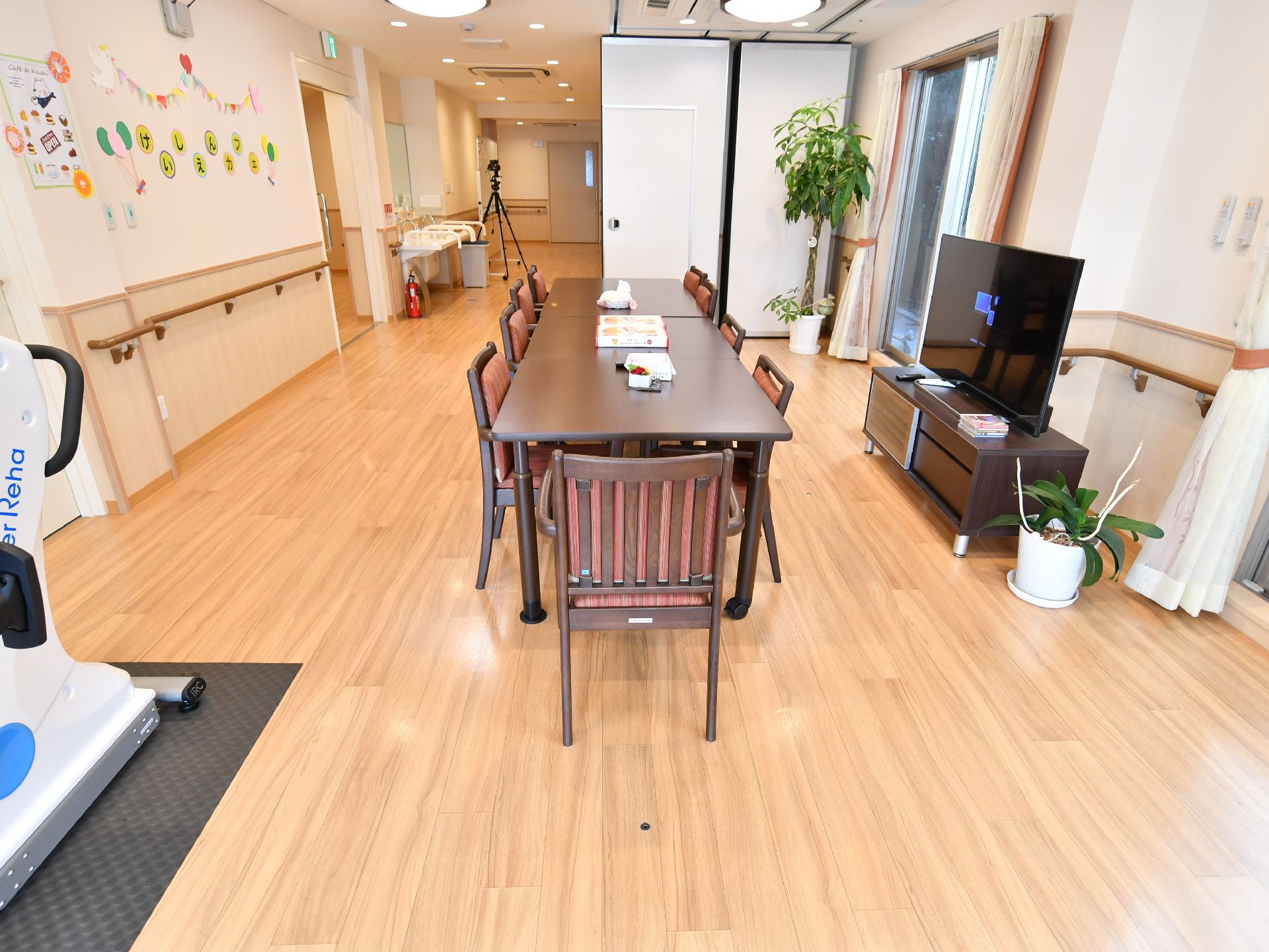 部屋は外の光が入り込み、明るく奥行きがある。中央にテーブルと椅子があり、近くに運動する機械とテレビが置かれている。
