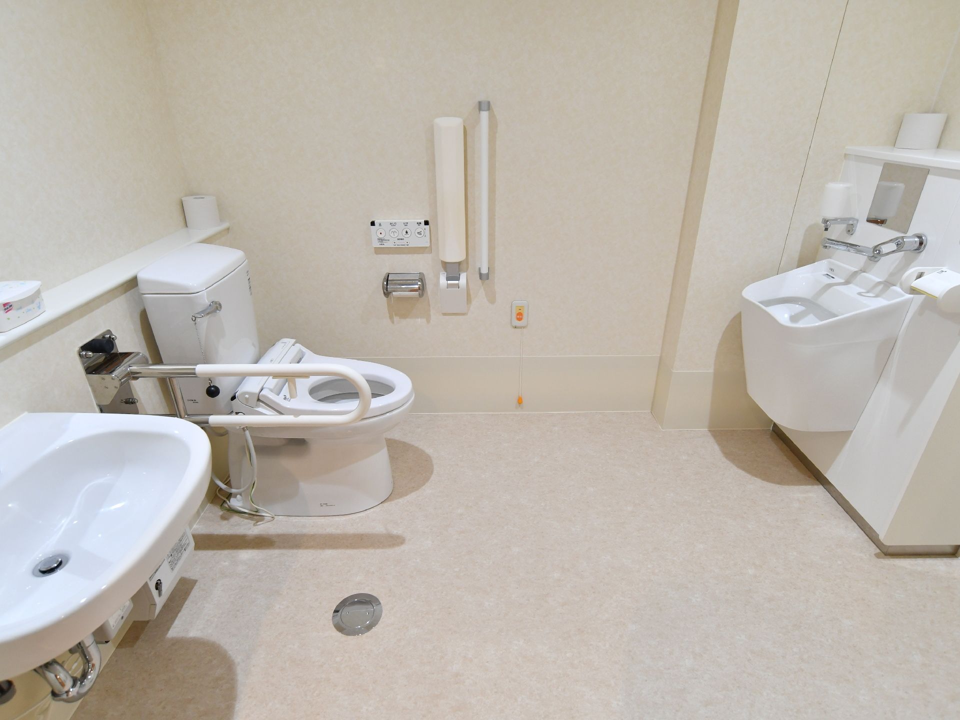 トイレの中は広々としている。便器の近くに手摺がある。お尻を洗う機能が備わっている。非常時用のボタンがある。