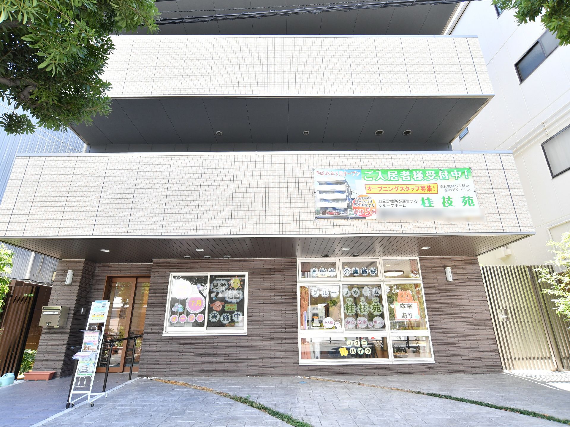 白色と茶系の外観の鉄筋コンクリート造4階建の施設で、建物の横側に玄関出入口がある。玄関前はアプローチになり横側に手すりがある。