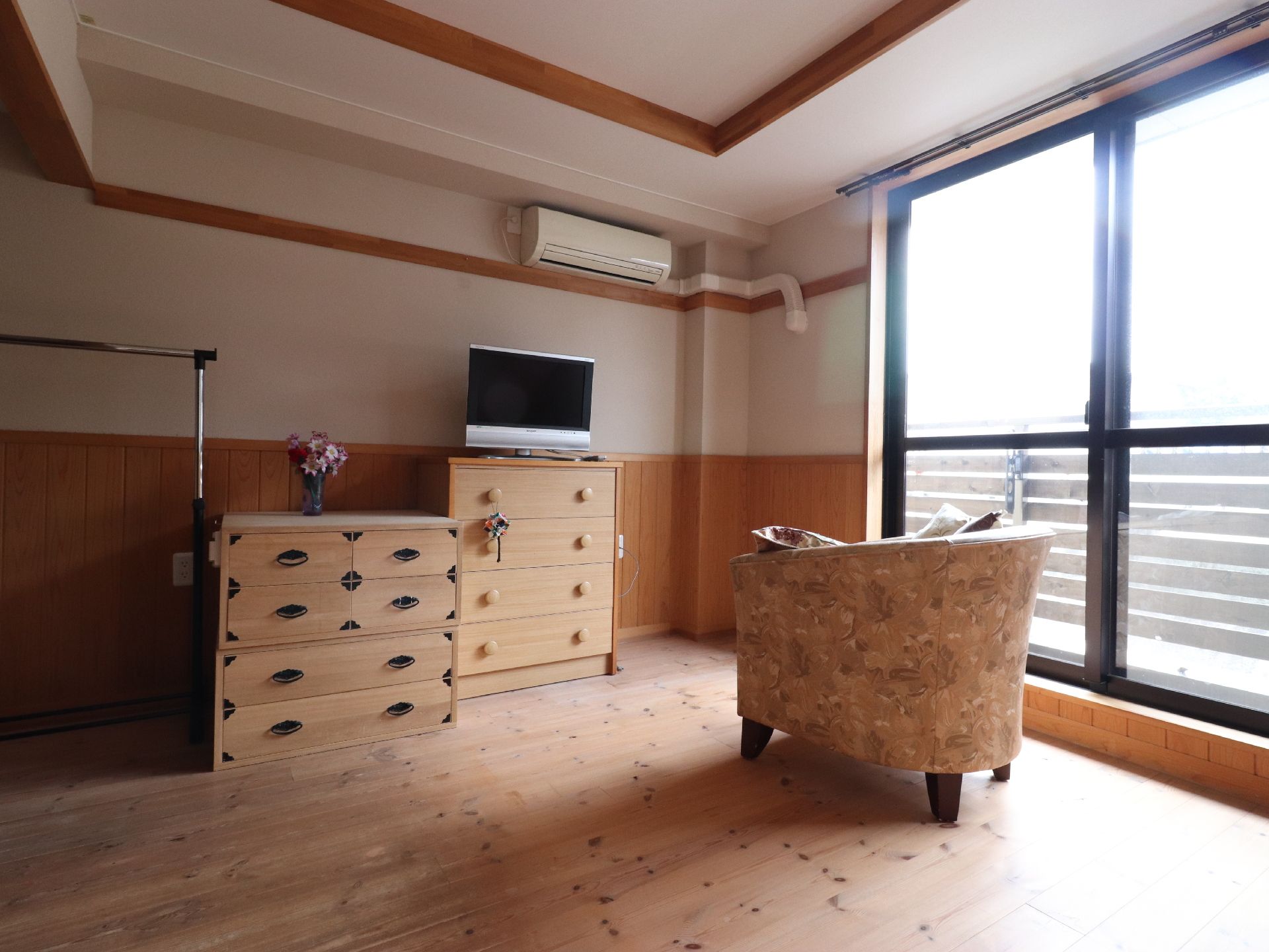 室内の壁は白と茶色の2色で構成されている。床はフローリングになっている。右側には掃き出し窓が設置されており、その奥にはベランダがみえる。