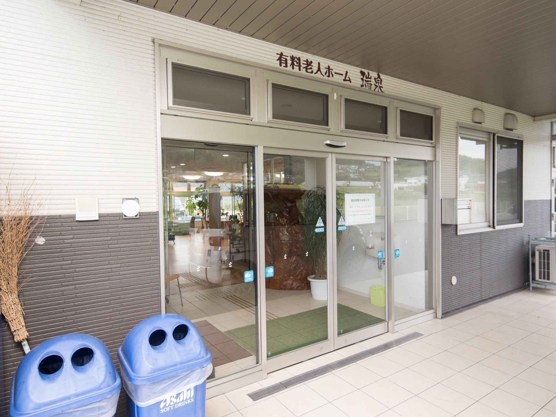 ガラス張りの自動ドアがある、中を見通すことができる広い玄関。施設の外壁は白と黒のツートーンになっている。