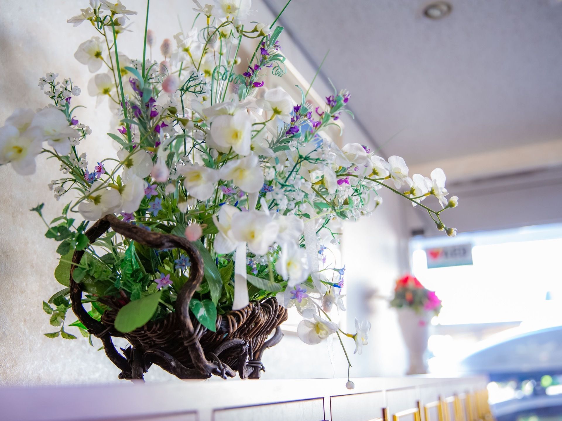 玄関の靴棚の上に、色とりどりの花が咲いている花束が蔓で編み上げられたベースに飾られている。花瓶に入った花束もある。