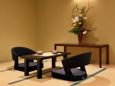 浴室の傍に畳のお部屋をご用意している。壁際の台の上に豪華な生け花を飾り、中央スペースにテーブルと座椅子を配置している。
